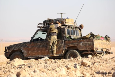 A soldier interacting with a camouflaged utility vehicle in the desert.