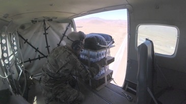 A solider pushing supplies out of an airborne vehicle.