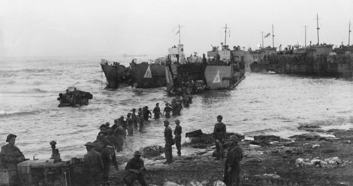 Just after dawn men of the Highland Division are up to their waists in water unloading stores from landing craft tanks. Meanwhile beach roads are being prepared for heavy and light traffic during dawn of the opening day of the invasion of Sicily.