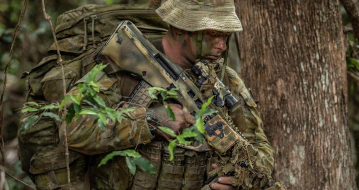 A soldier analyses the terrain before them as they make their way through the woods.