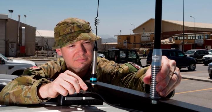 Australian Army officer Major Geoffrey Small installs a silver shield electronic countermeasure device on a vehicle.