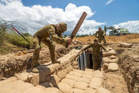 A sapper tamps sandbags during trench construction.