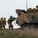 Australian Army soldiers conducting a dismounted section attack from an Armoured Personnel Carrier.