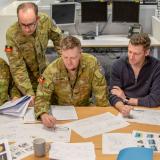 Soldiers seated around a table strewn with papers.