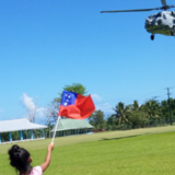 A child waves a Samoan flag at a landing helicopter.