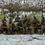 An Army officer addressing soldiers under camouflage netting and over a very large map on the ground.