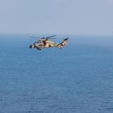 Helicopters fly in formation above the ocean.