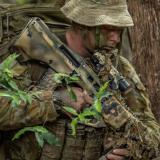 A soldier analyses the terrain before them as they make their way through the woods.
